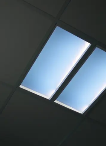 Moderne Deckenbeleuchtung mit bläulichem Licht, das an Tageslicht erinnert, in rechteckigen Panels integriert.