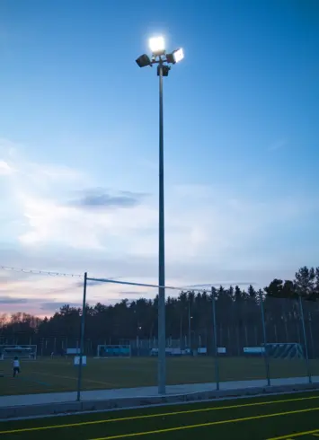 Flutlichtmast mit mehreren LED-Strahlern, die den Sportplatz in der Abenddämmerung beleuchten.