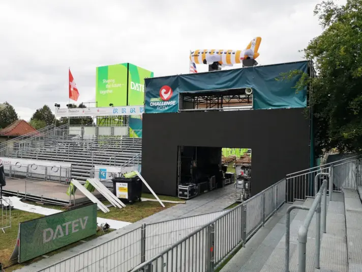 Tribüne und Eventbühne mit DATEV- und Challenge Roth-Branding, bereit für eine Veranstaltung, mit einem aufblasbaren Condor-Flugzeug auf dem Dach.