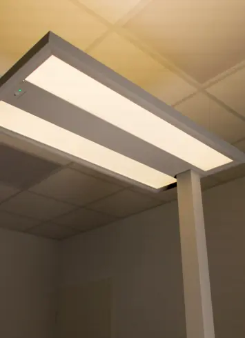 Beleuchtetes LED-Stehleuchtenpanel in modernem, minimalistischem Design, montiert in einem Büro mit Rasterdecke. Die Lampe strahlt warmweißes Licht aus.