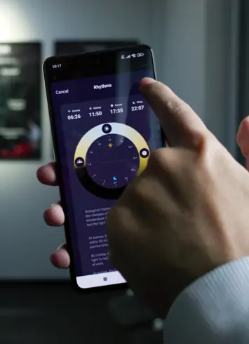 Person bedient Smartphone mit einer App zur Steuerung biologischer Rhythmen, einschließlich Sonnenaufgang, Sonnenuntergang und Schlafenszeit.